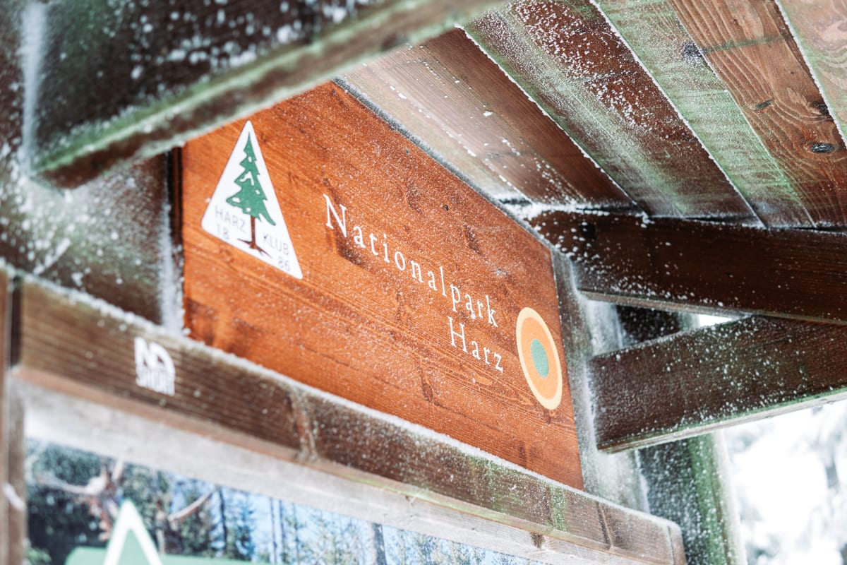 Schneebedecktes Holzschild des Nationalparks Harz unter einem hölzernen Dach.