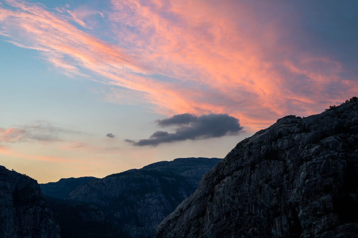 Pink and orange clouds above dark, jagged rock faces at sunset.