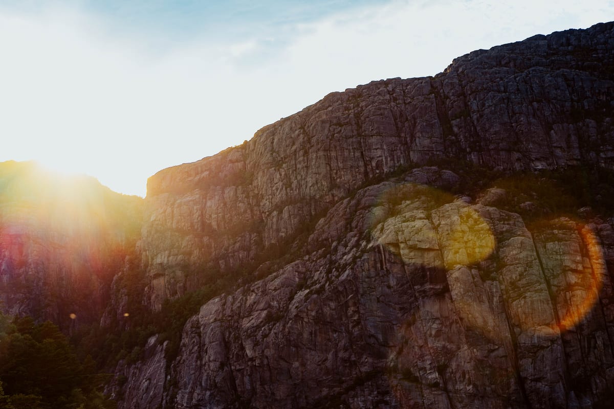 Tief stehende Sonne hinter einer geschichteten Felswand mit Lichtreflexen über der felsigen Landschaft.