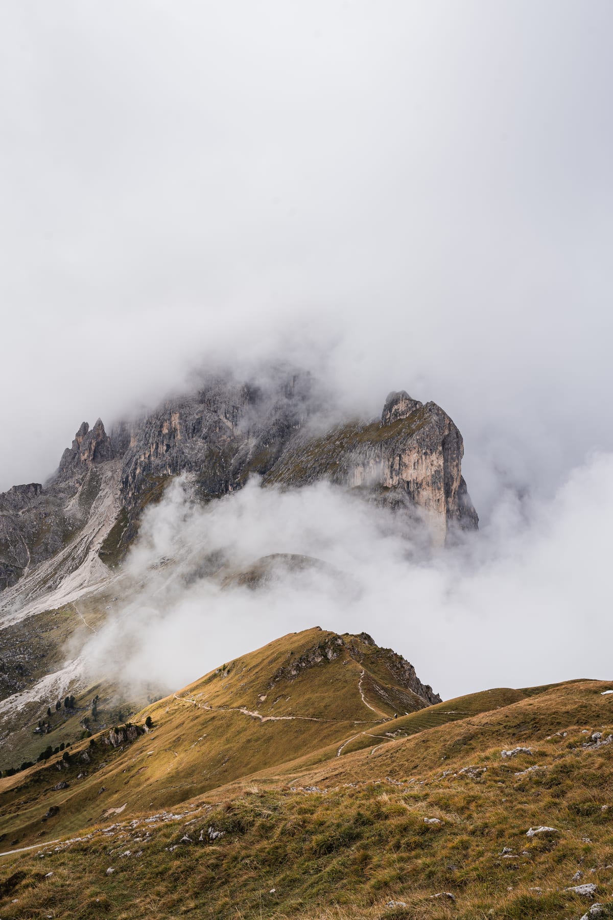A grassy ridge beneath steep rock faces partly hidden by clouds.