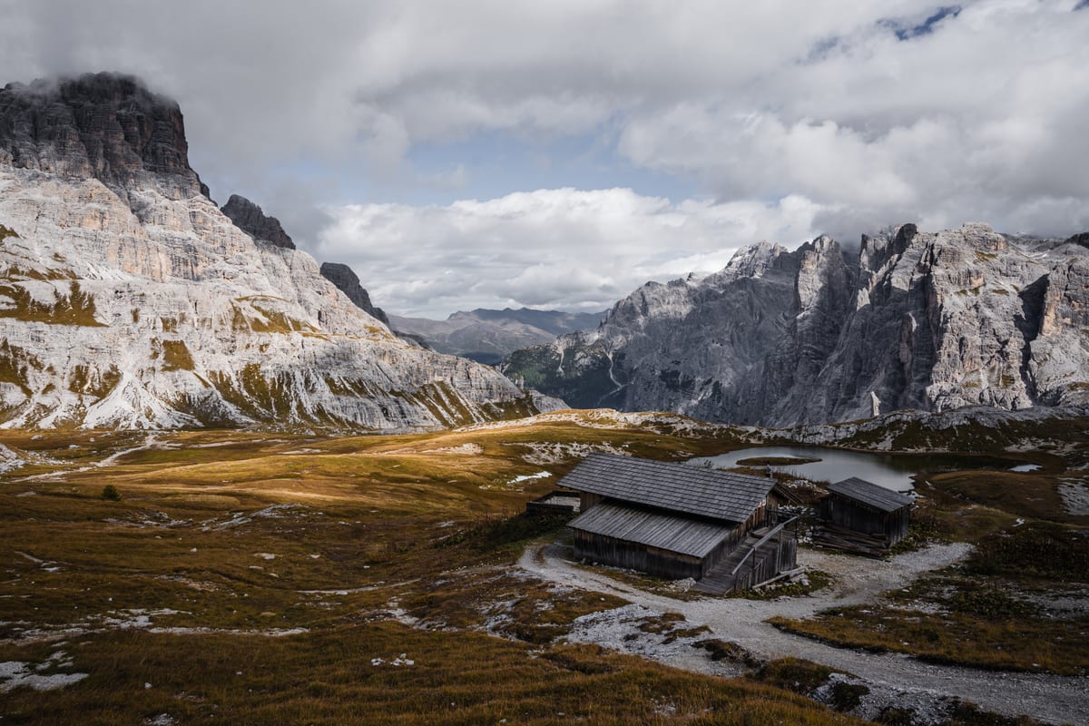 Wooden huts on a sparse plateau between steep rock faces under a cloudy sky.