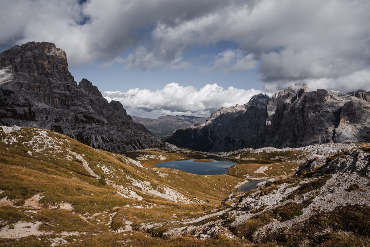 A mountain lake in a broad rocky basin surrounded by grassy slopes and tall rock faces.