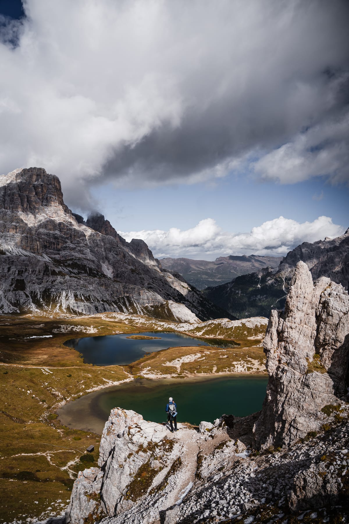 Two small mountain lakes among pale rocks and golden-brown meadows beneath dark clouds.